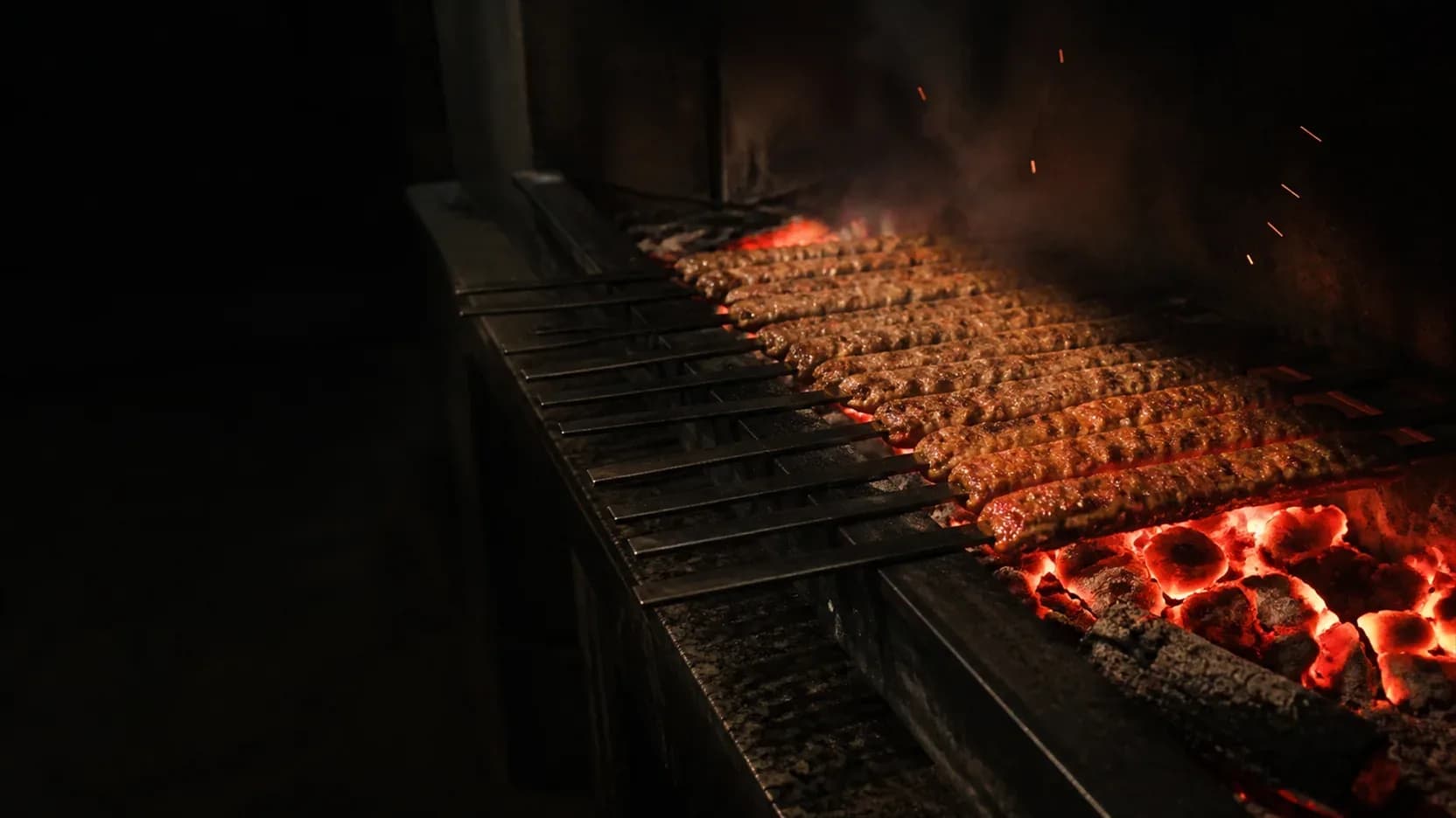 Uzun mangalda sıra sıra adana kebap şişleri, kıvılcımlar havada